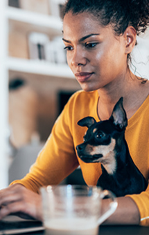 Uma mujer con su pequeño perro escribiendo en su computadora portatil